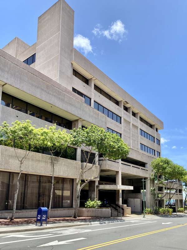 Built in 1960, this Brutalist building was constructed as the headquarters of the Hawaii National Bank.  The building features a rough textured concrete exterior, boxy geometric forms, a protruding parapet on the exterior facing walls, ribbon