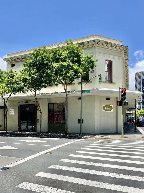 Built in the early 20th Century, this Classical Revival-style commercial building, featuring a stucco clad-exterior, bracketed cornice, and arched one-over-one double-hung windows, is a contributing structure in the Chinatown Historic District,