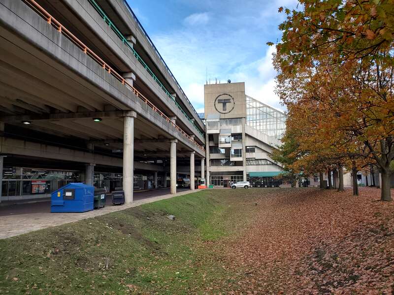 The east side of the parking garage, with the busway underneath, at Alewife station in November 2020. In the foreground is the artificial pond created as part of Richard Fleischner's 1985 environmental artwork. Behind is the tower of elevators,