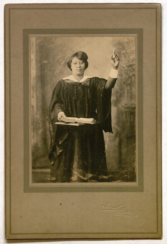 Card mounted photo of a woman in black religious robes reading from a book atop a pedestal. The card is imprinted with the logo of Fowler Photography Studio formerly at 238 N. 8th Street in Philadelphia, Pennsylvania.