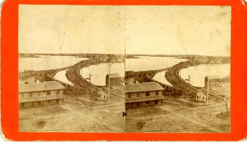 Aerial view looking toward the North River at the Eastern Railroad tracks, which appears to have been taken from the back of one of the courthouses on Federal Street. Train cars are visible along with the &quot;Lowell &amp;amp; Northern R.R. Depot&quot; building,