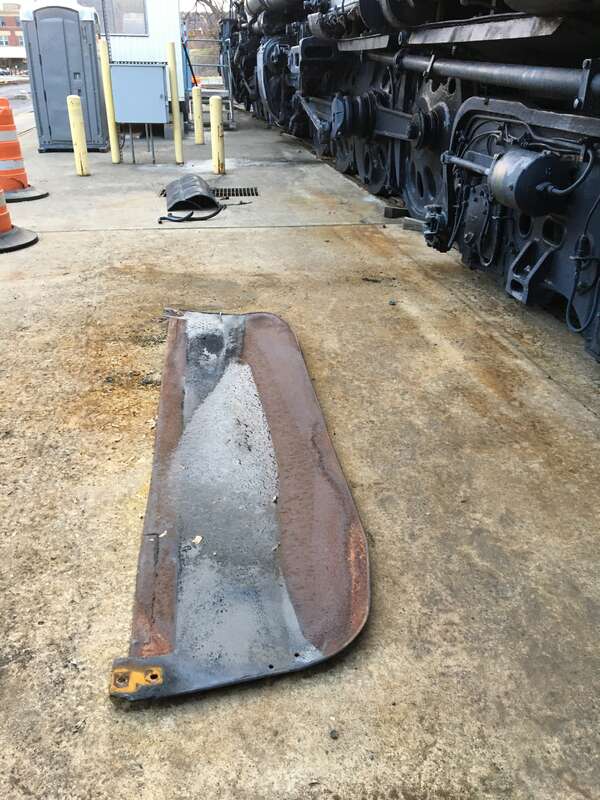Various metal pieces from the locomotive laying on a concrete floor next to the locomotive.
Along with the tender, separate parts of the locomotive were sandblasted. These parts are the aprons of the ashpan, which were removed from the outer edges of