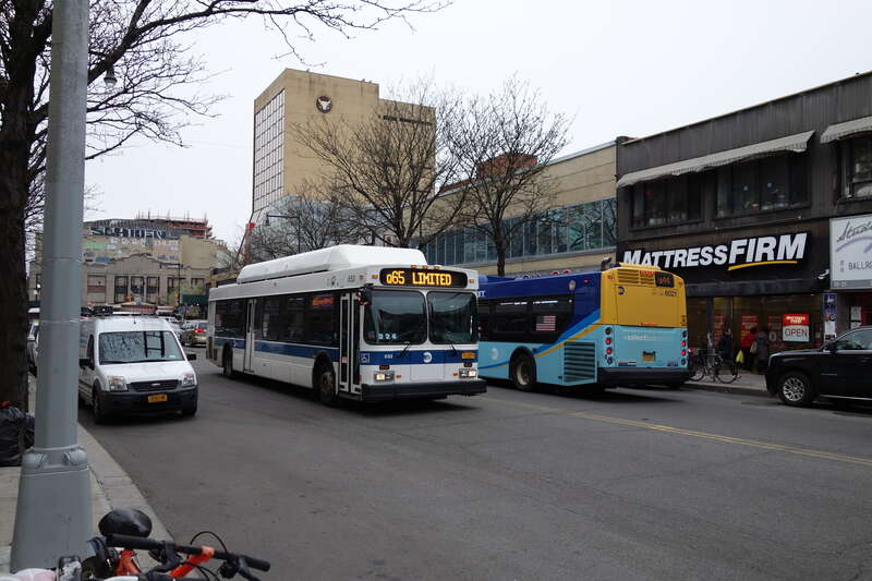 A Jamaica LIRR-bound Q65 Limited bus traveling south, and a Bronx-bound Q44 SBS bus traveling north, on Main Street between Northern Boulevard and 37th Avenue in Downtown Flushing, Queens.