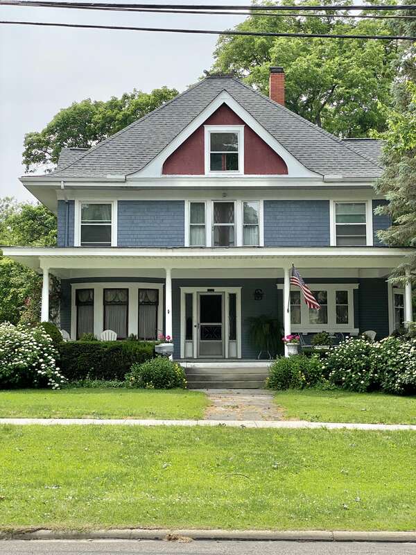 Built around the turn of the 20th Century, this Queen Anne-style house features a shingle and clapboard exterior with a hipped roof featuring a flared lower portion and broad overhanging eaves, stucco-clad gables on the front and side facades,