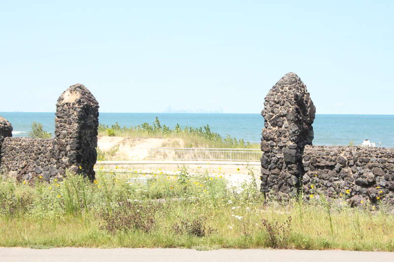 Lake Michigan shoreline in Marquette Park, Gary, Indiana.  The Chicago skyline is visible in the distance across the lake, framed by the old stone gate.