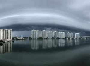 A shelf cloud (a type of arcus cloud) reflecting on Dumfoundling Bay in northeastern Miami-Dade County, Florida. Apartment buildings in Aventura, Florida are visible on the other side of the bay.