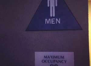 A sign stating the maximum occupancy of a men's restroom.