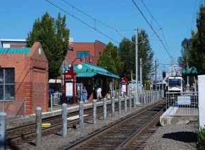 The MAX light rail station at TriMet's Gresham Central Transit Center, viewed from the west.  An outbound train is pulling away from the platform (this is the rear of the train).  Mount Hood is visible in the distance.The building at left was